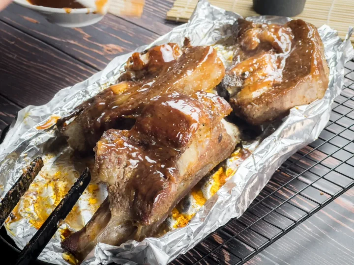 Oven-baked beef slathered with BBQ sauce on a baking tray lined with aluminum foil.