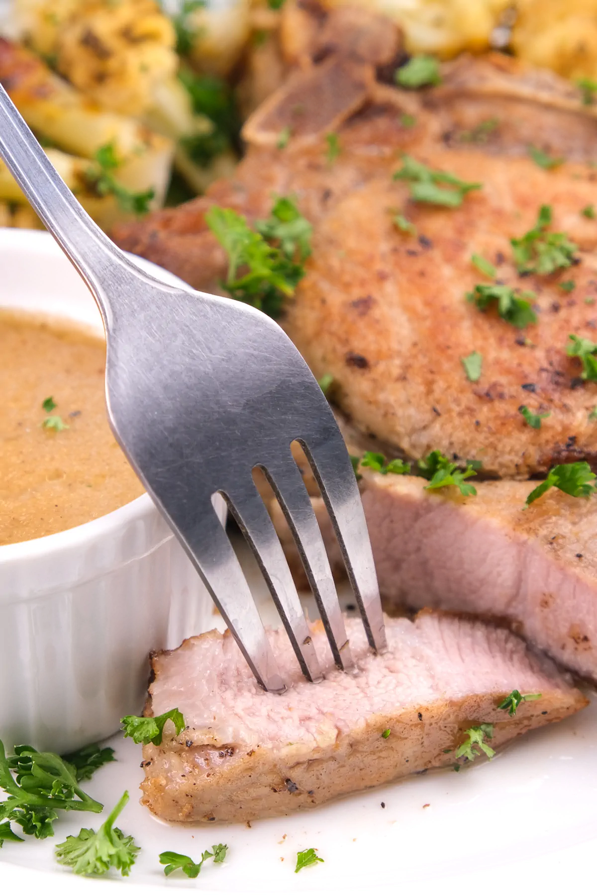 Keto oven-baked bone-in pork chops plated, with a fork bearing a small portion.