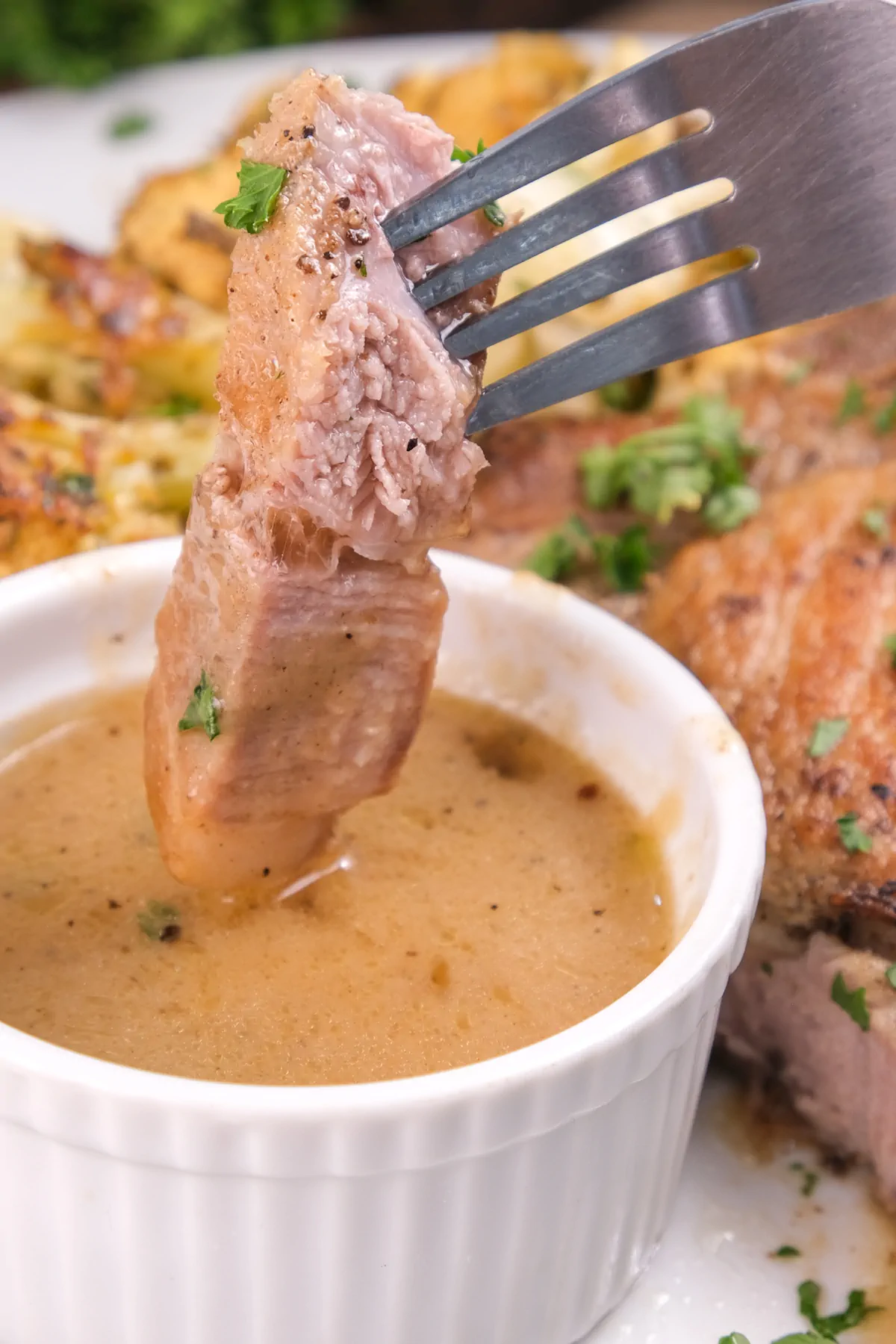Dipping a small portion of pork chops in a sauce in a small bowl with a fork.