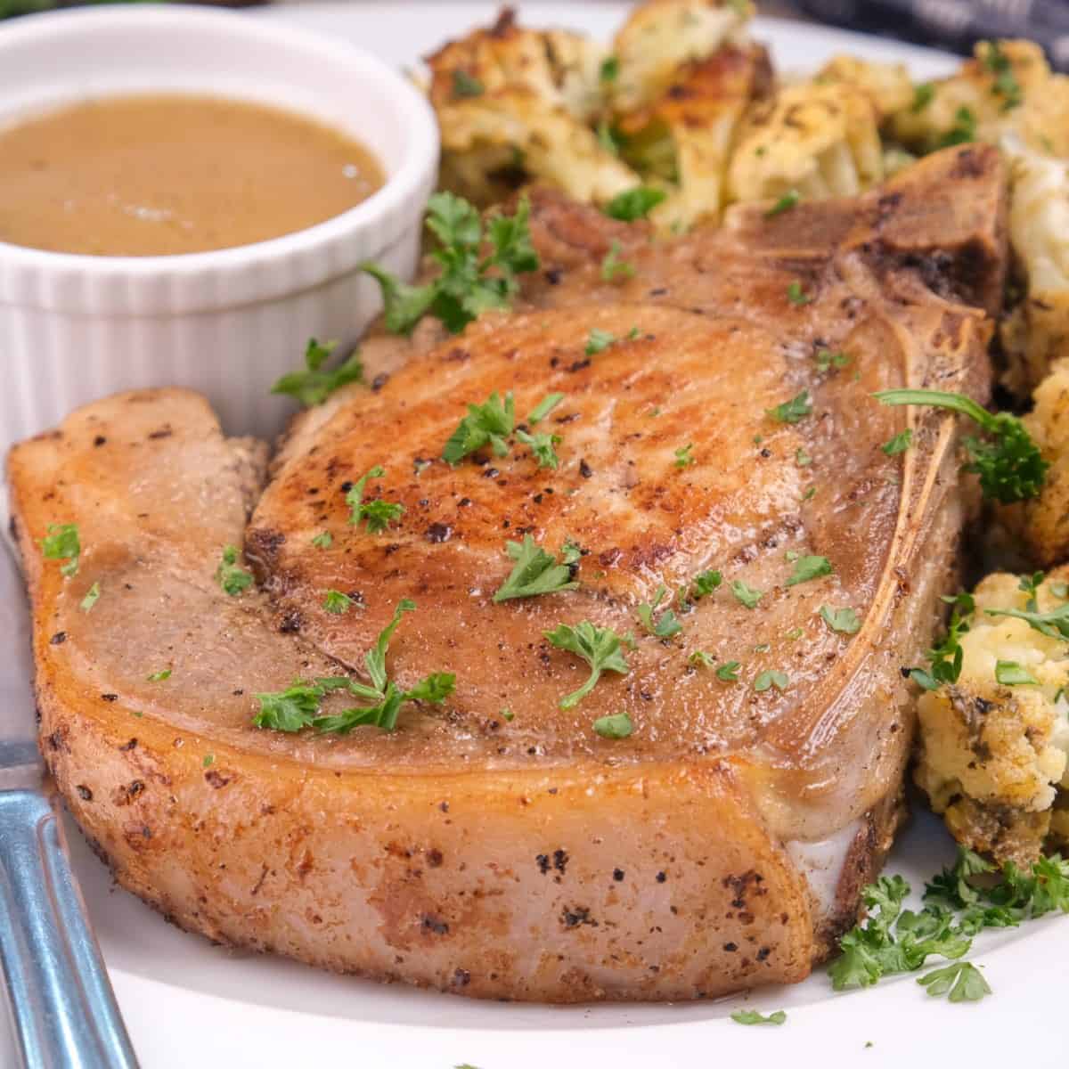Keto oven-baked bone-in pork chops recipe served with a sauce.
