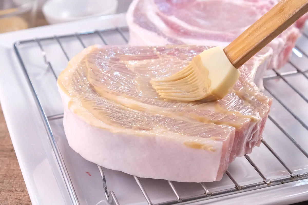 Brushing the bone-in pork chops with Dijon mustard.