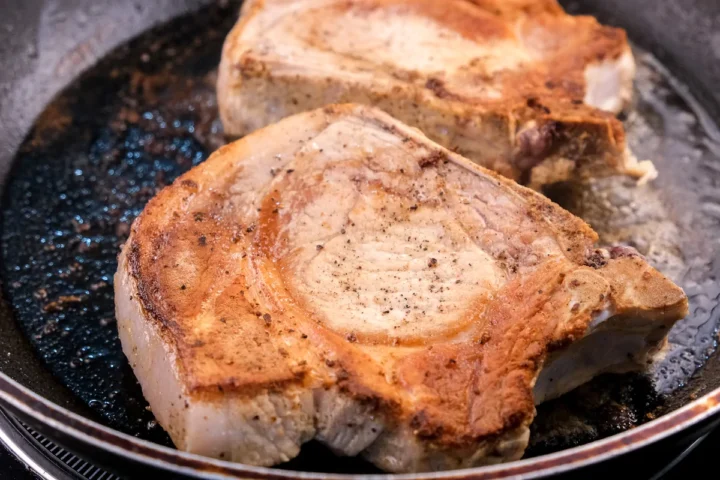 Searing the pork chops on high heat in a pan.