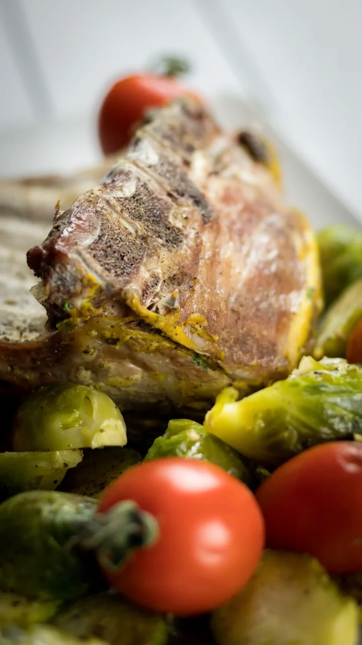 Focused picture of oven-roasted rack of lambs served with Brussel sprouts and cherry tomatoes.