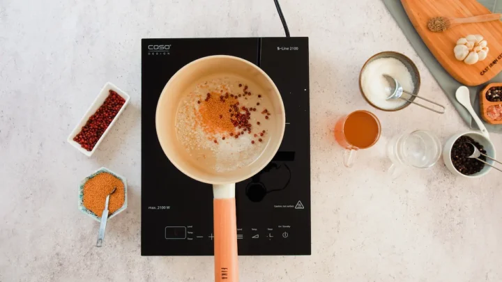 Pickling salt, red peppercorns, and mustard seeds are in a saucepan on an induction top.