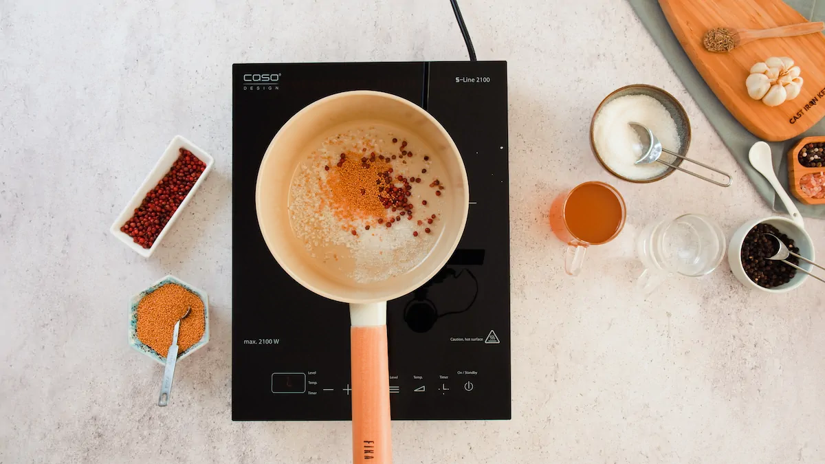Pickling salt, red peppercorns, and mustard seeds are in a saucepan on an induction top.