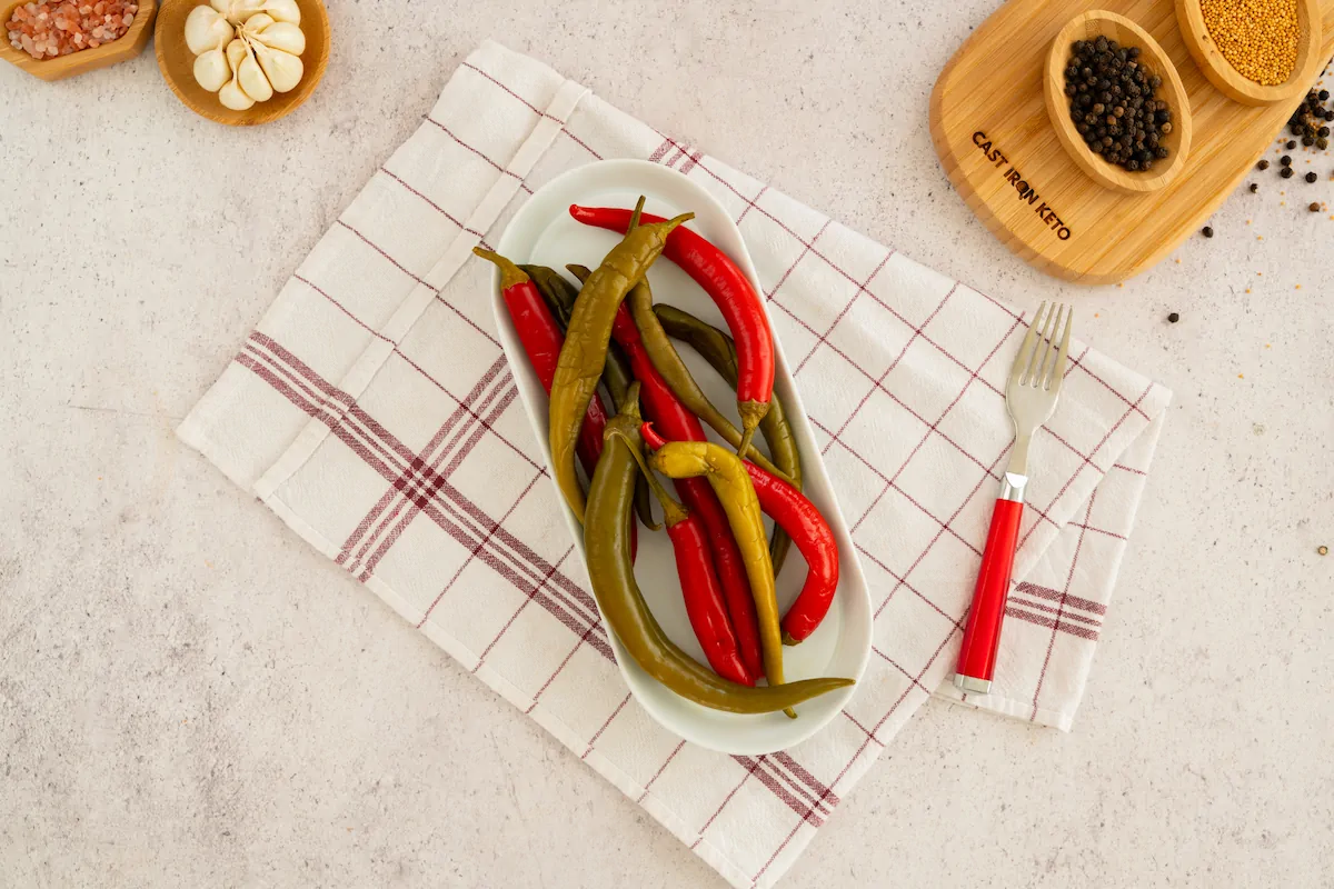 Homemade pickled peppers served on a plate alongside a fork.