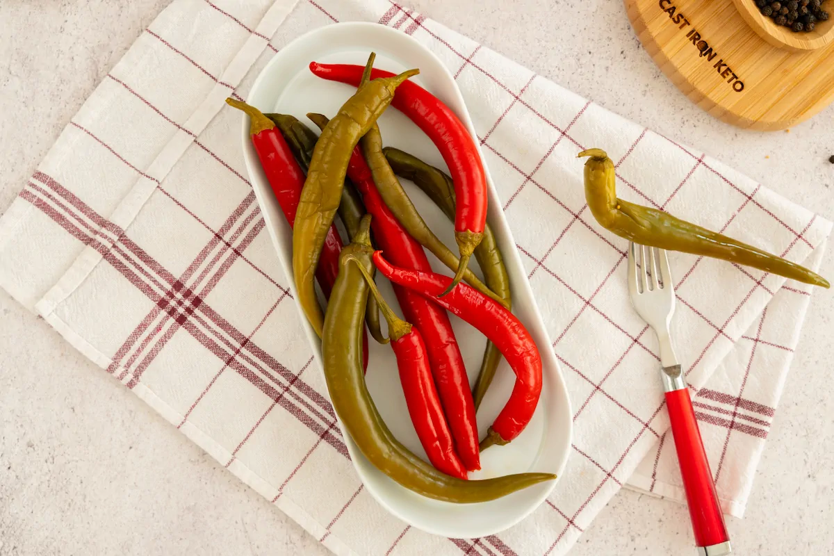 Pickled peppers served on a plate alongside a fork with a pepper.