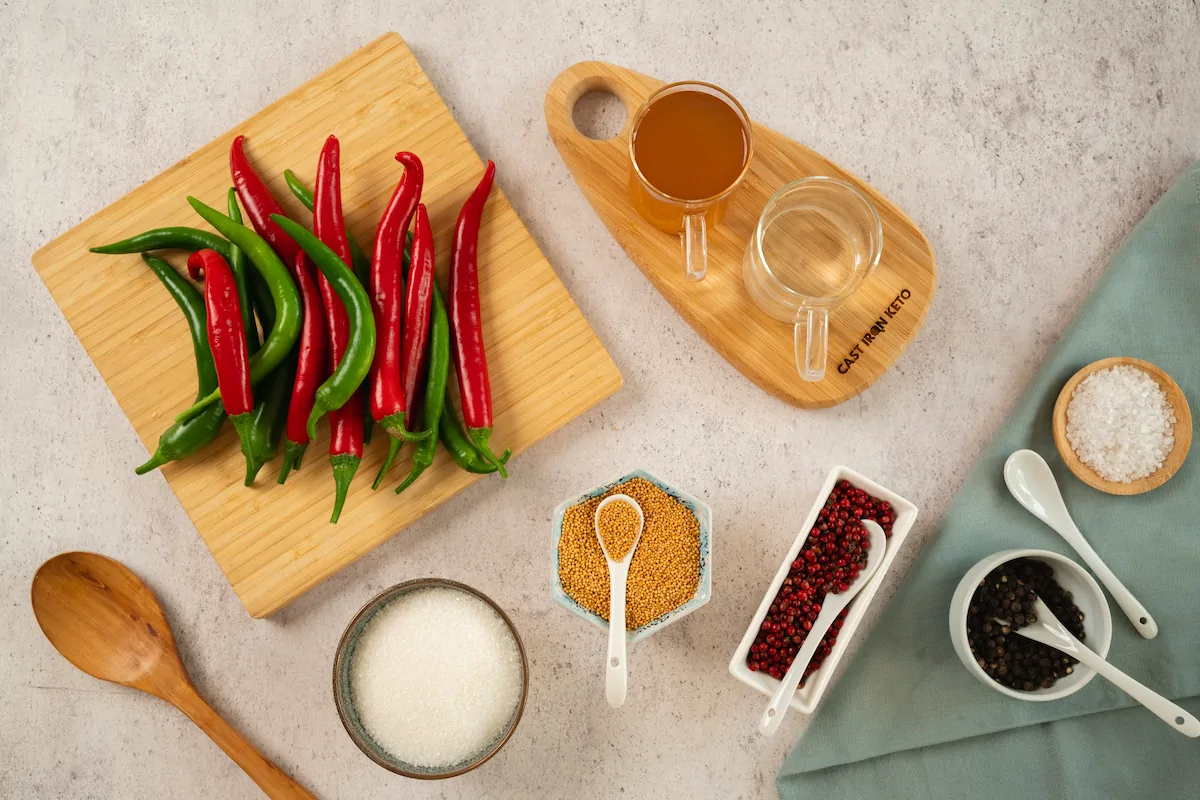 All the ingredients required to make pickled peppers including chili peppers, water, apple cider vinegar, pickling salt or sea salt, whole black peppercorns, mustard seeds, red peppercorns, keto-friendly sweetener gathered and displayed on the table.