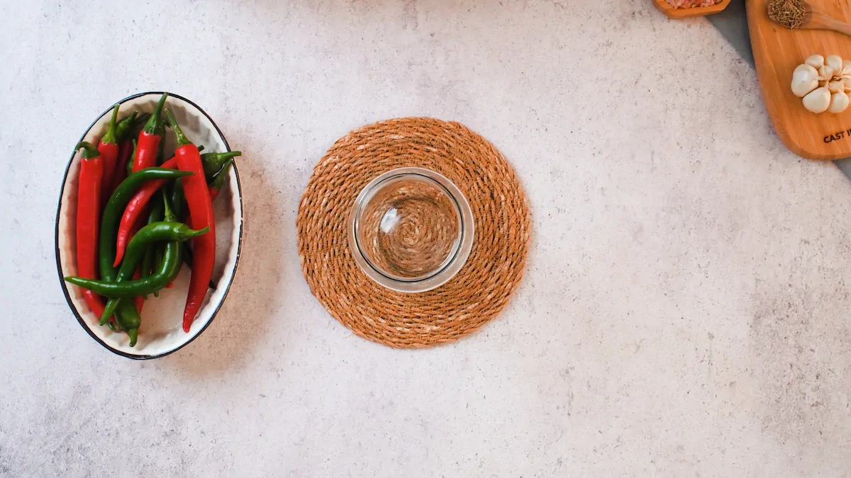 An empty glass jar alongside a bowl of red and green peppers.