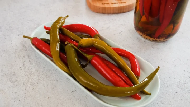 Pickled peppers served on a plate beside the jar of the same pickles.