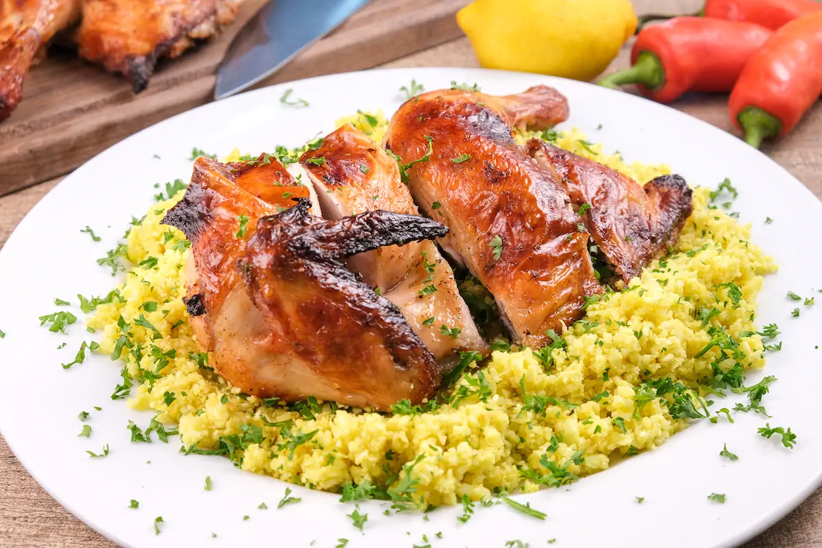 Keto pollo asado served on a bed of cauliflower rice and garnished with fresh herbs.
