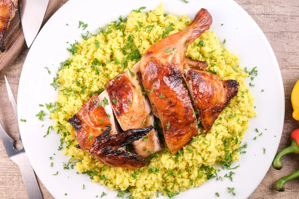 Low-carb pollo asado plated over cauliflower rice and garnished with fresh herbs.