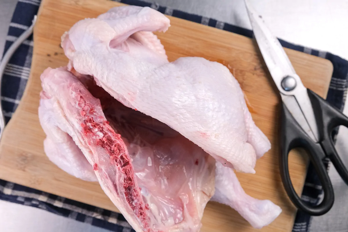 Chicken cut into two halves on a chopping board with a pair of scissors.