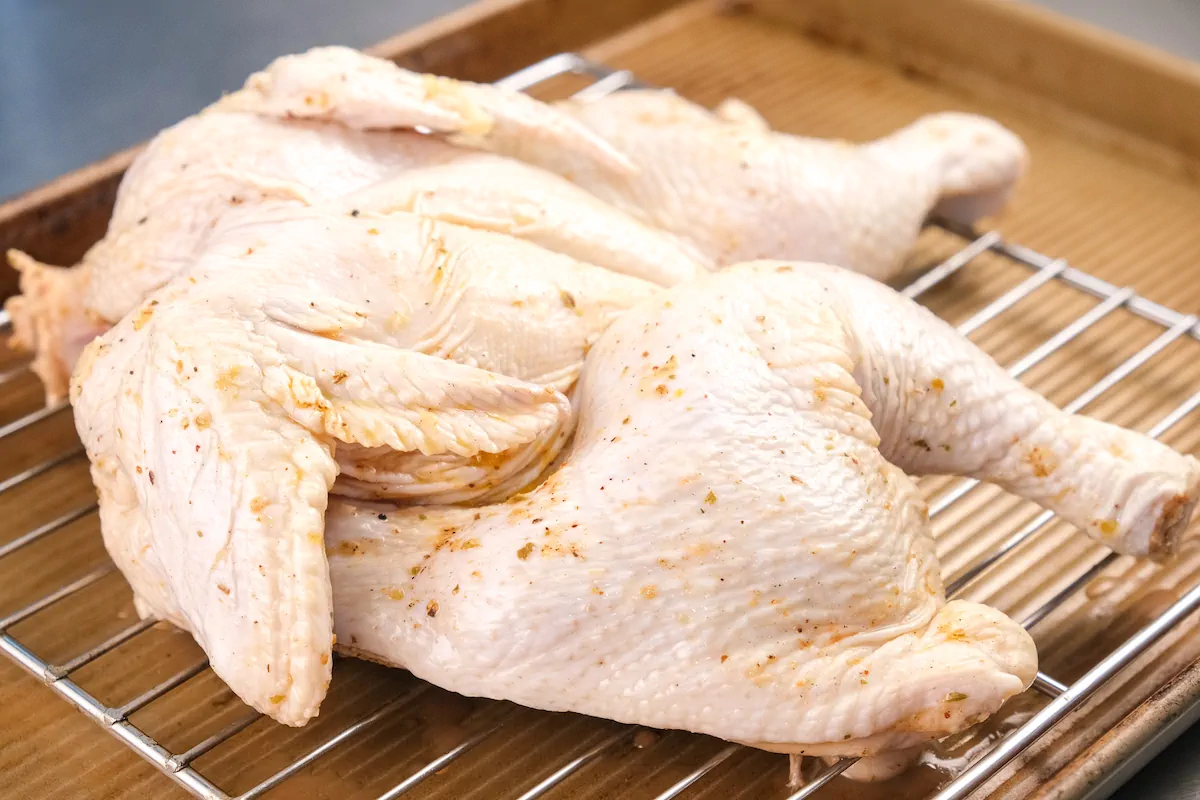 Raw spatchcock chicken on a wire rack ready to be roasted.
