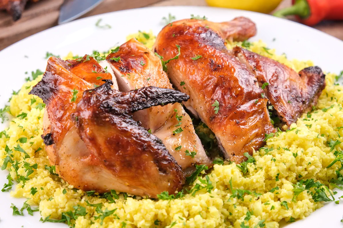 Low-carb pollo asado plated on cauliflower rice, garnished with fresh herbs.