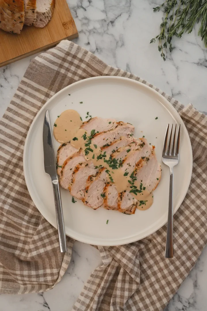 Sliced roasted turkey breast poured with keto gravy, served on a plate.