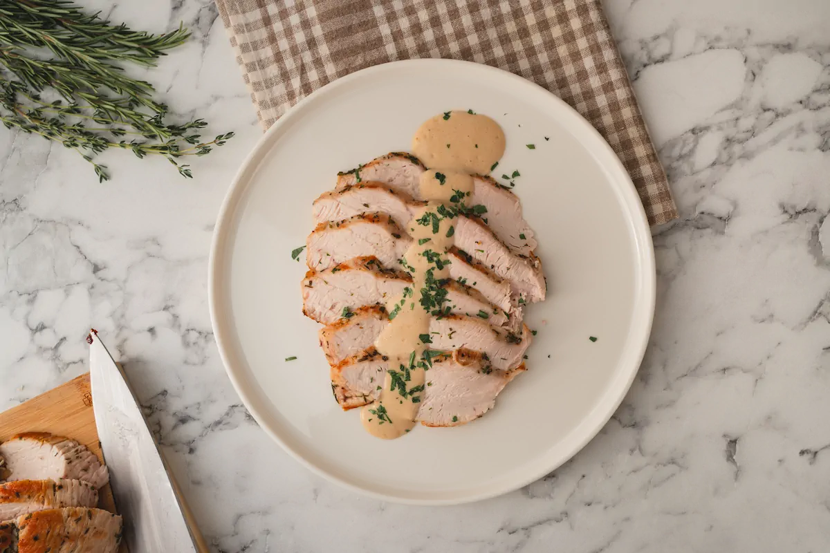 Slices of turkey breast with keto gravy poured on top and garnished with fresh herbs.