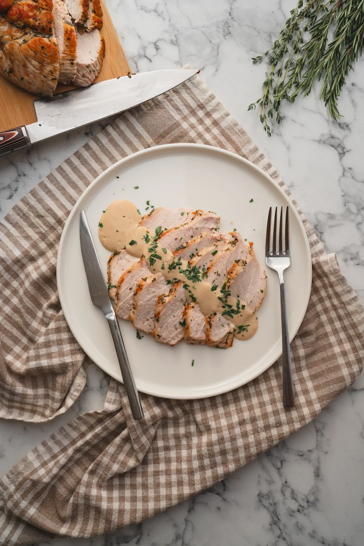 Turkey breast, roasted and sliced, topped with keto gravy on a plate with a fork and a knife.
