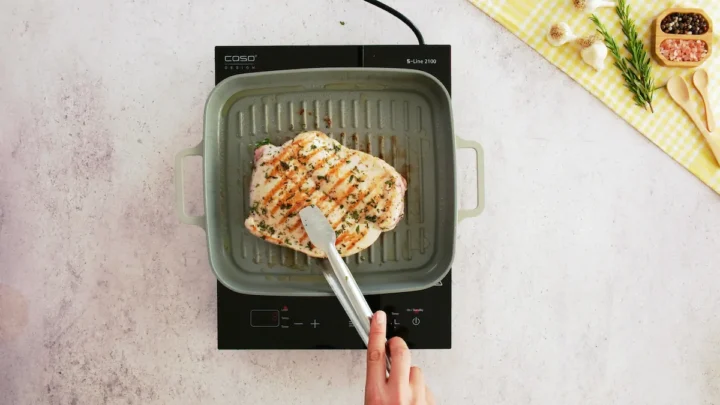 Turning turkey breast with tongs cooking in a grill pan, it has golden grill marks on top.