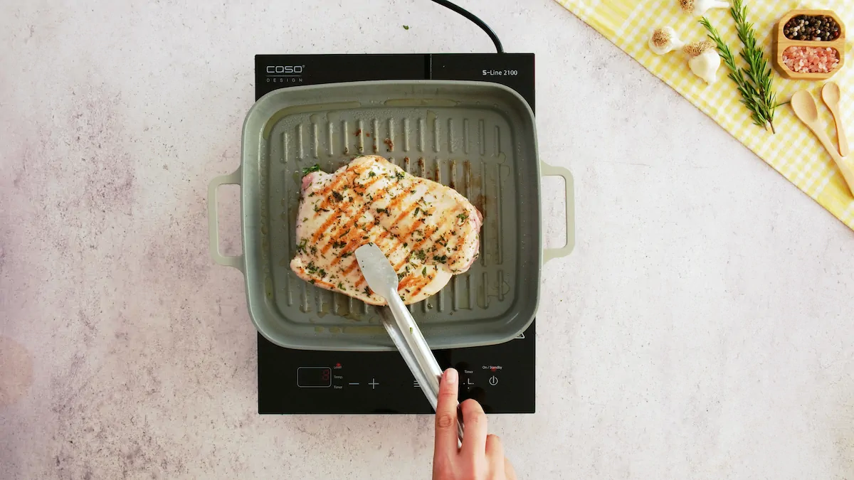 Turning turkey breast with tongs cooking in a grill pan, it has golden grill marks on top.