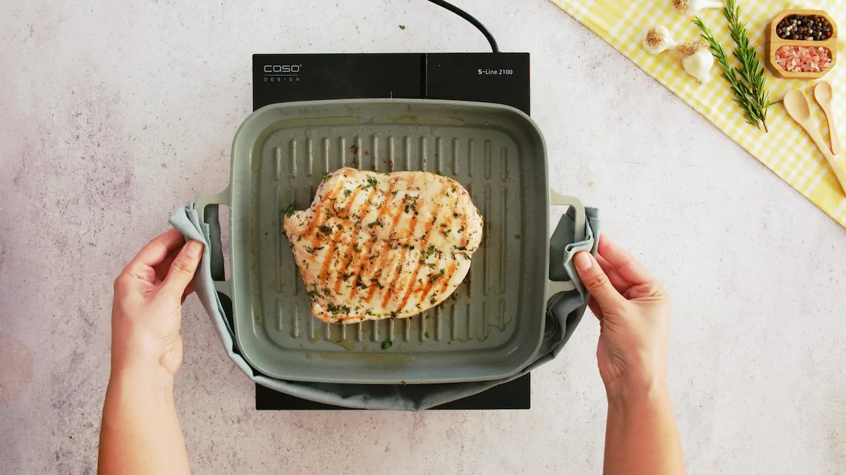 Hands holding a grill pan with turkey breasts.
