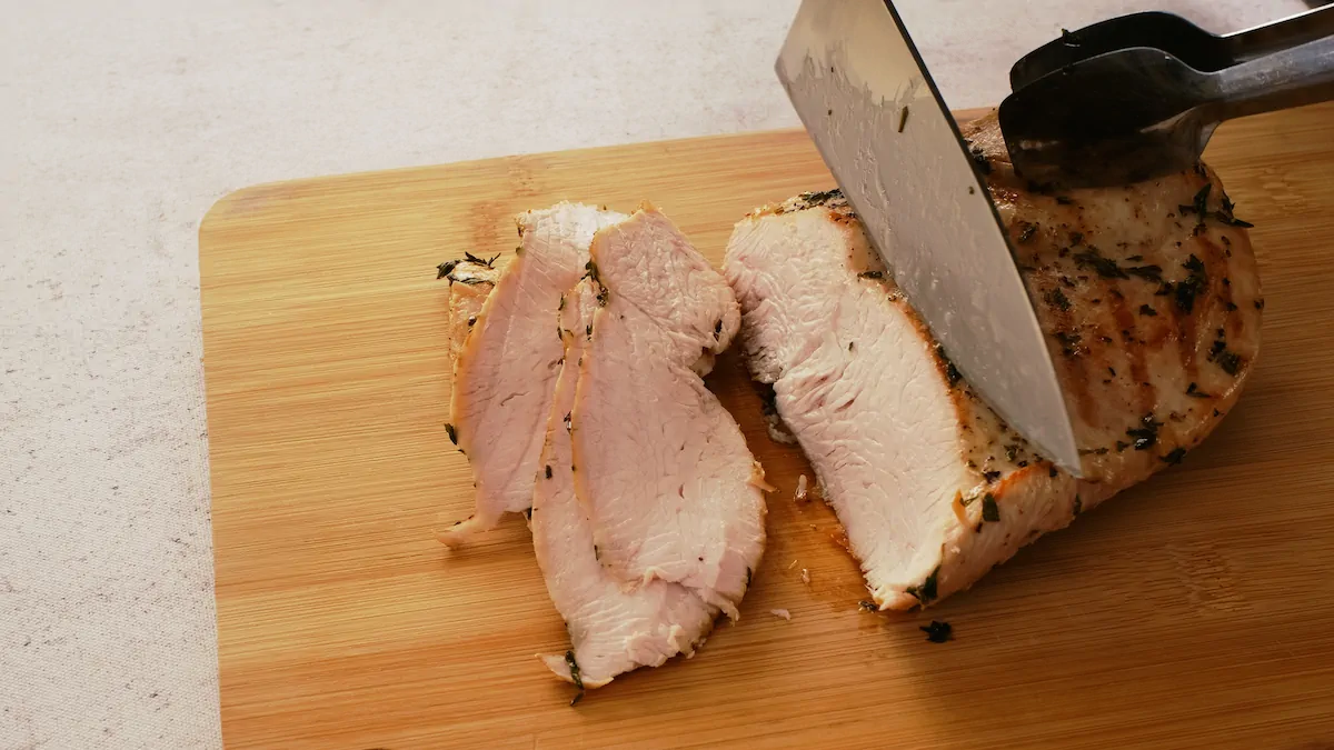 Roasted turkey breast getting sliced with a knife on a wooden chopping board.