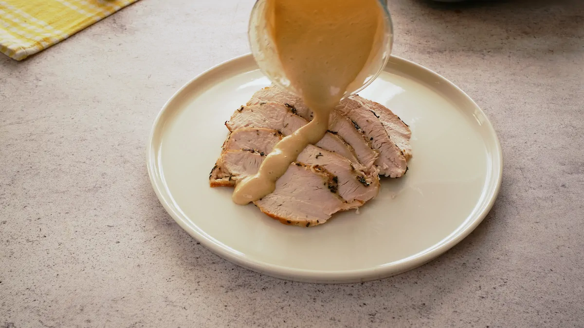 Pouring keto gravy on slices of roasted turkey on a plate.