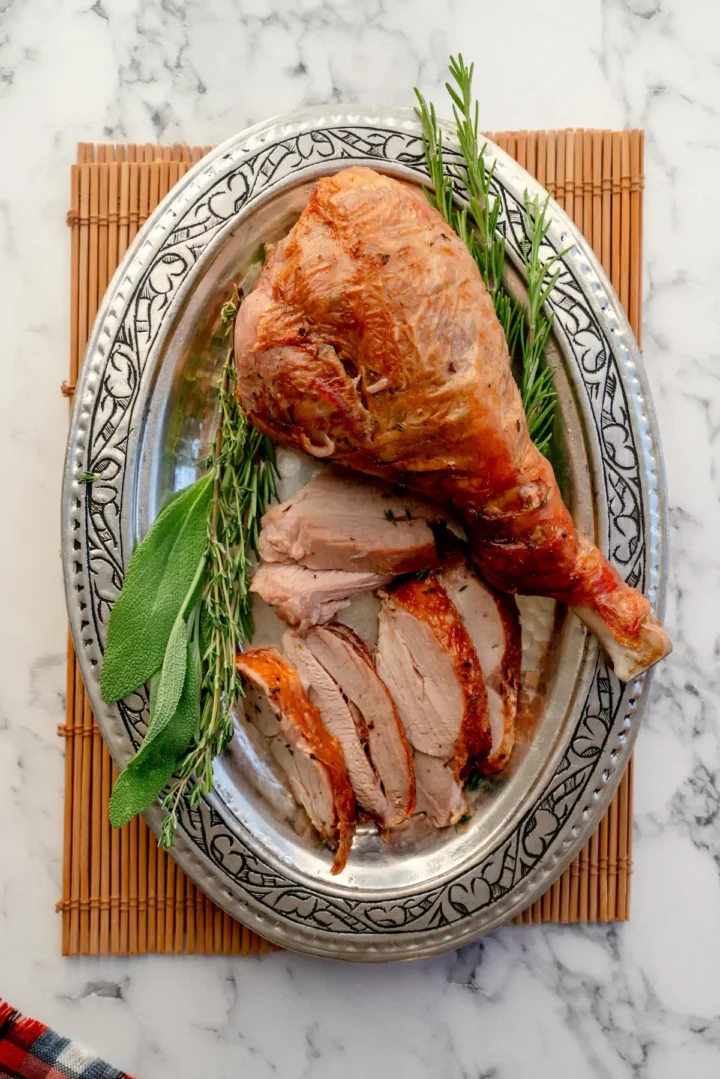Sliced roasted turkey leg with a drumstick served on a plate.