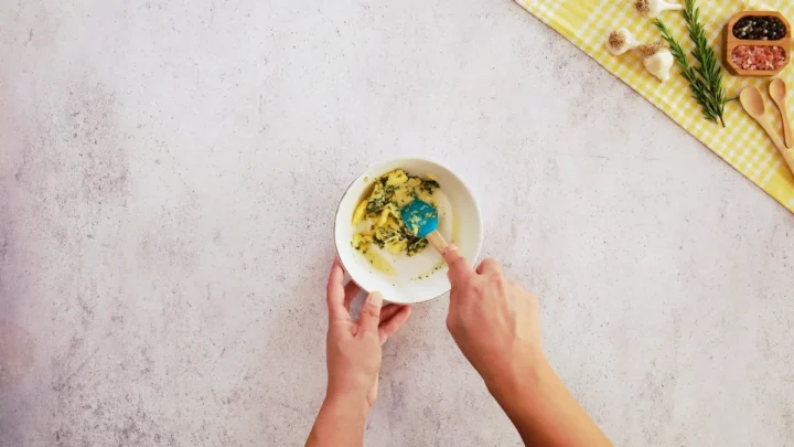 Herbs are mixed with soft butter using a silicone spatula.