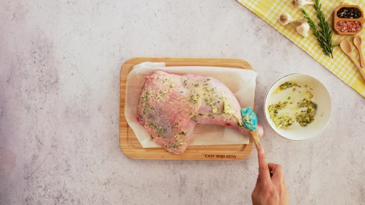 Rubbing the butter mixture over the turkey leg with a silicone spatula.