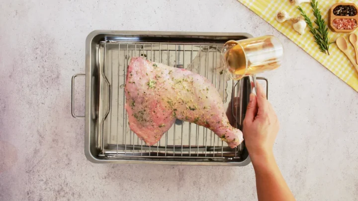 Turkey is placed on a roasting rack with a pan, and broth is poured into the roasting pan.