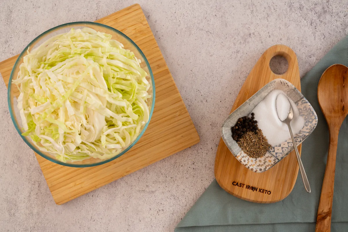The ingredients to make sauerkraut including medium green cabbage, sea salt, caraway seeds, black peppercorns arranged and displayed on the table.
