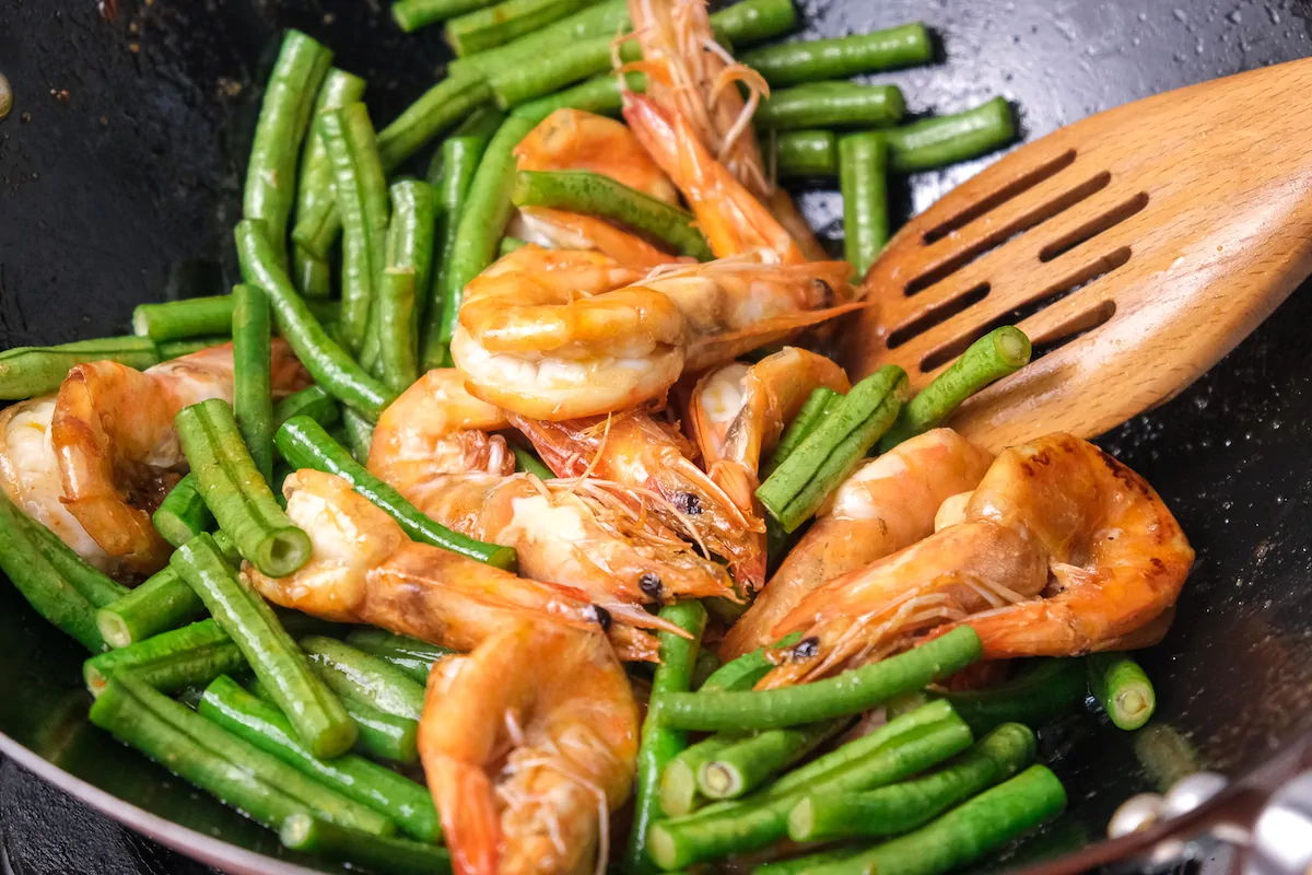 Shrimps getting cooked with string beans in a wok.