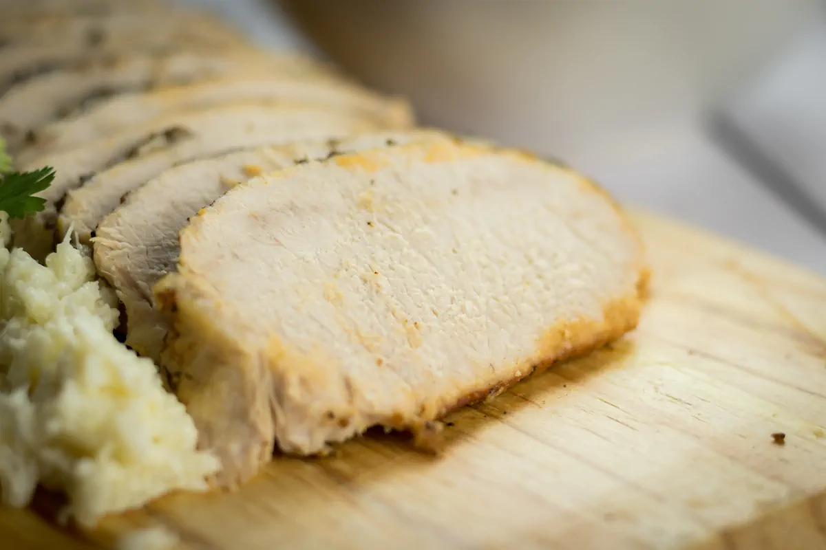 Focused shot of slow-cooked pork loin revealing its texture on a wooden board.