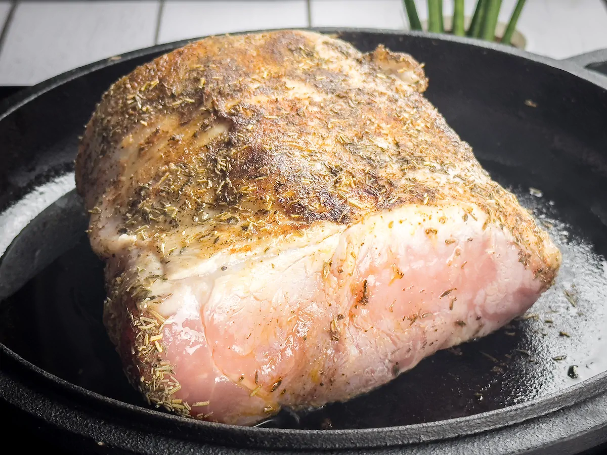 Pork loin getting seared on a cast iron skillet.