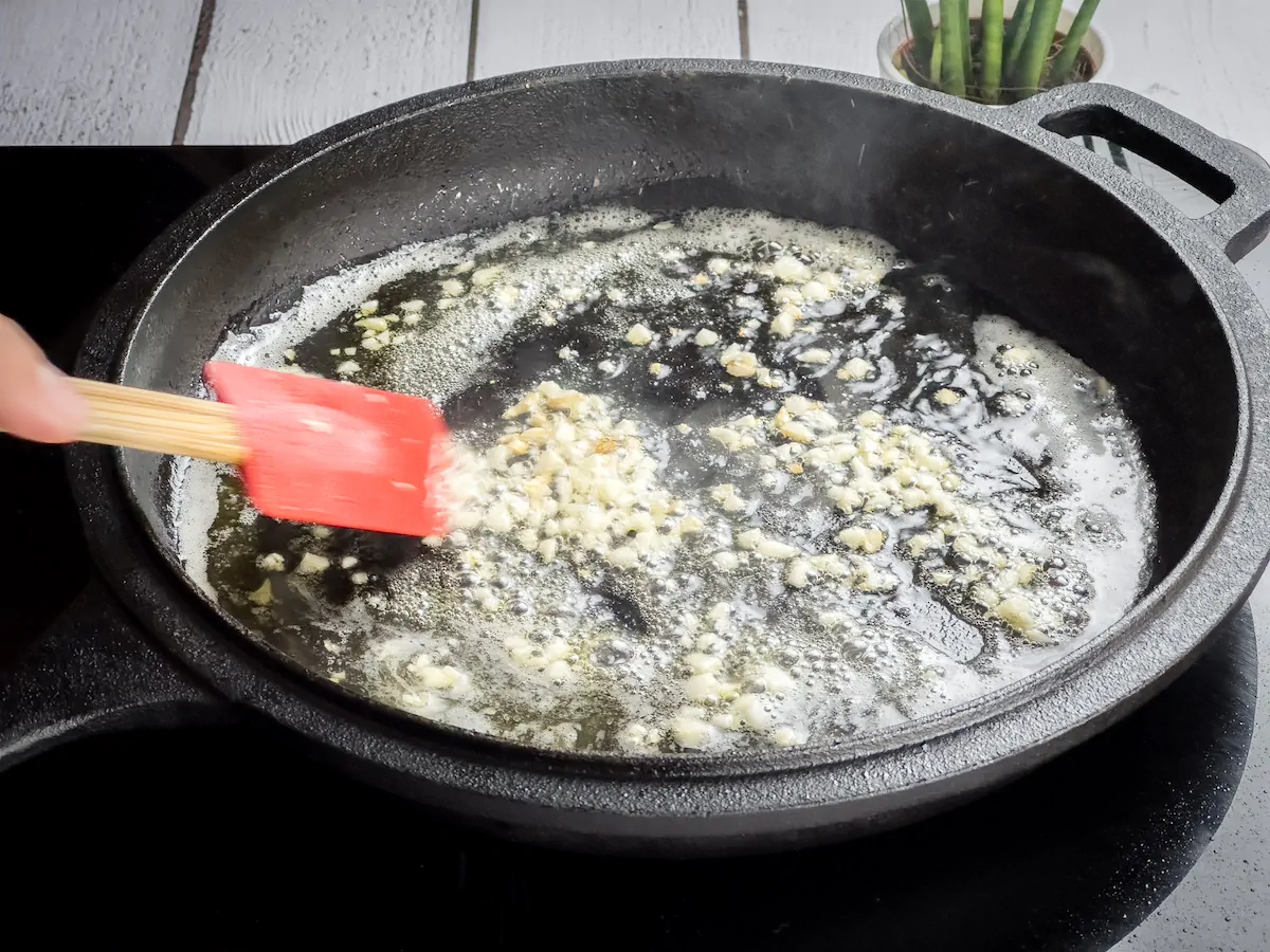 Sautéing minced garlic in butter in a cast iron skillet and stirring it with a silicone spatula.