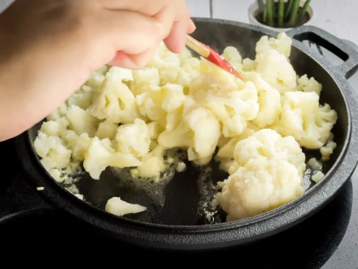 Stirring the steamed cauliflower florets in a cast iron skillet with sautéd garlic in butter.