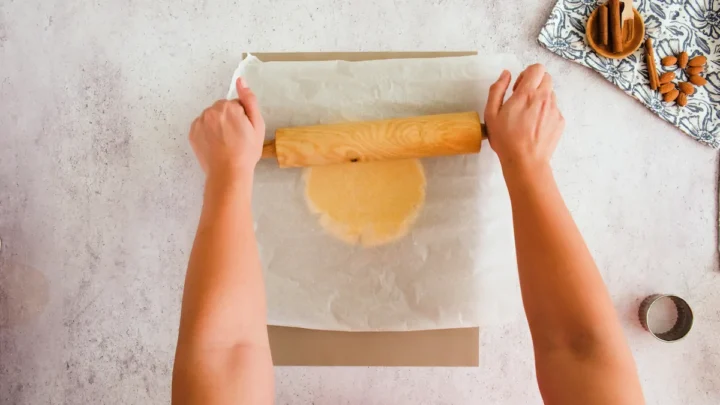 Rolling out the dough between the sheets of parchment paper with a rolling pin.