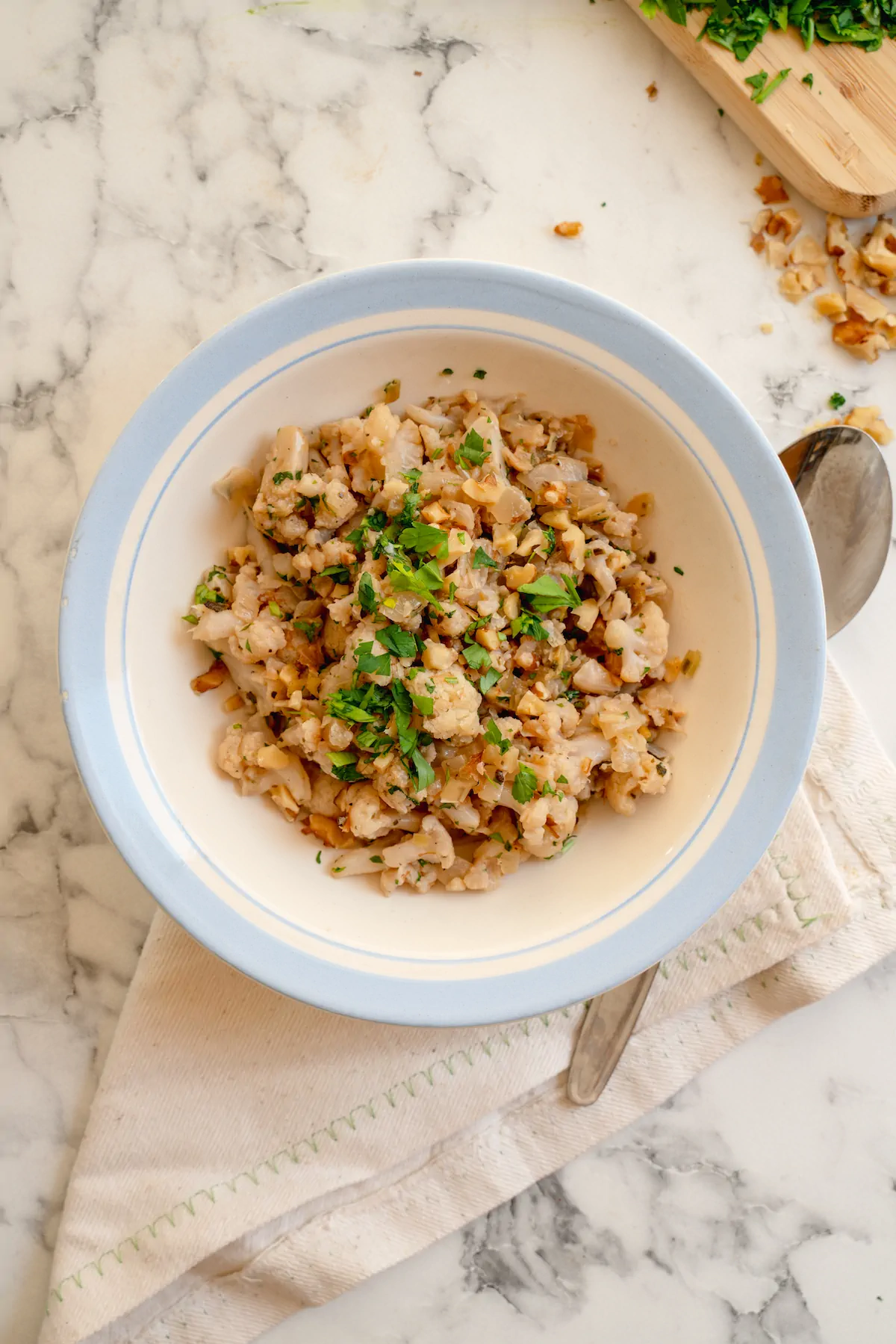 Low-carb cauliflower stuffing garnished with fresh herbs in a bowl alongside a spoon.