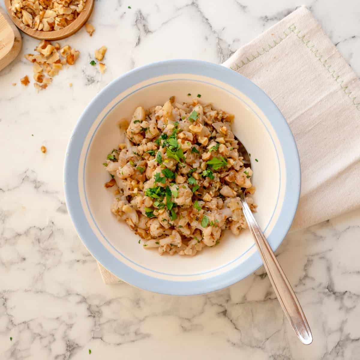 Cauliflower stuffing garnished with fresh herbs served in a bowl with a stainless steel spoon.