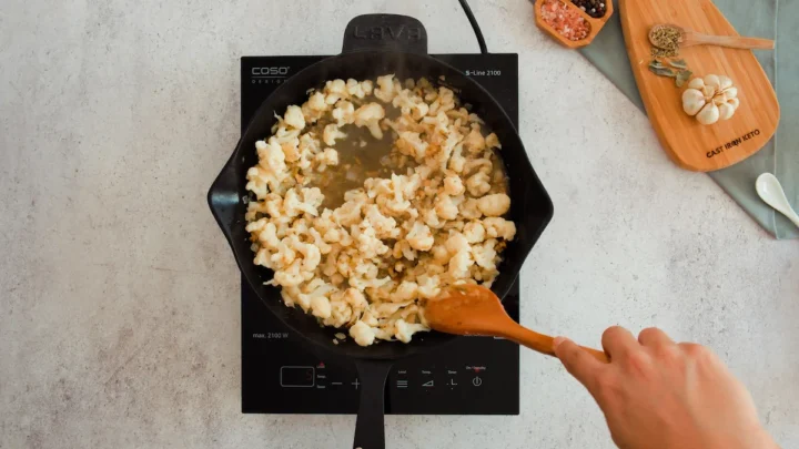 Mixing the cauliflower florets with broth in a cast iron skillet.