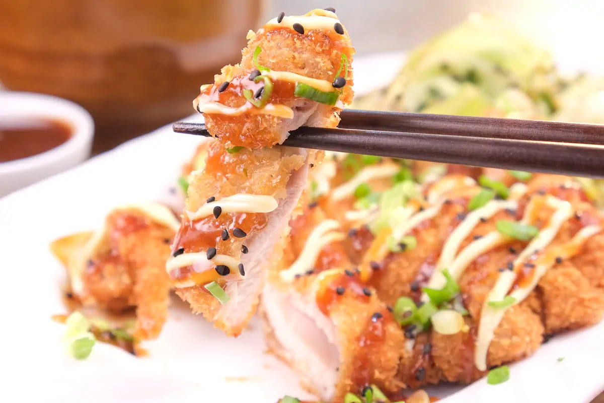 Holding a slice of chicken katsu with a pair of chopsticks.