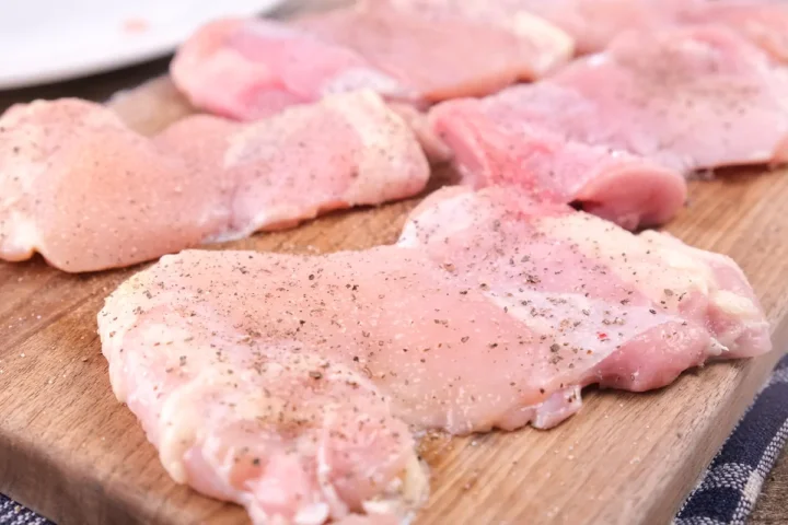 Seasoned chicken fillets are kept on a chopping board.