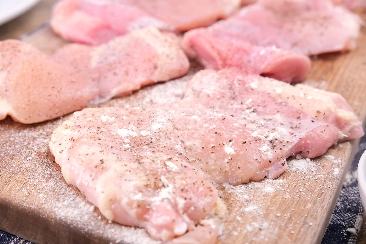 Chicken fillets sprinkled with protein powder on the wooden board.
