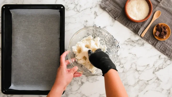 Mixing the dough for keto bounty bars with hands wearing gloves.