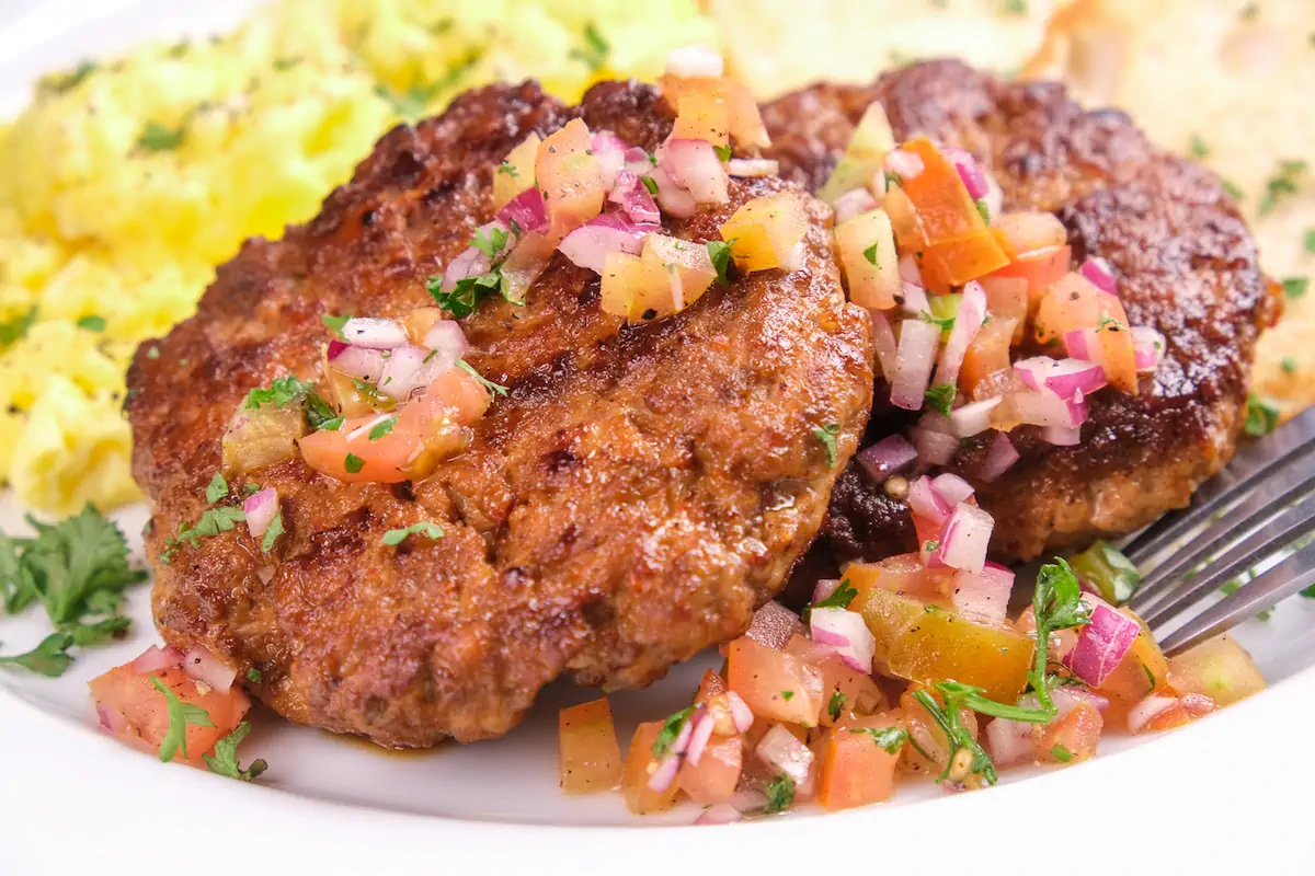 An up-close shot of keto breakfast sausage topped with diced onions and tomatoes.