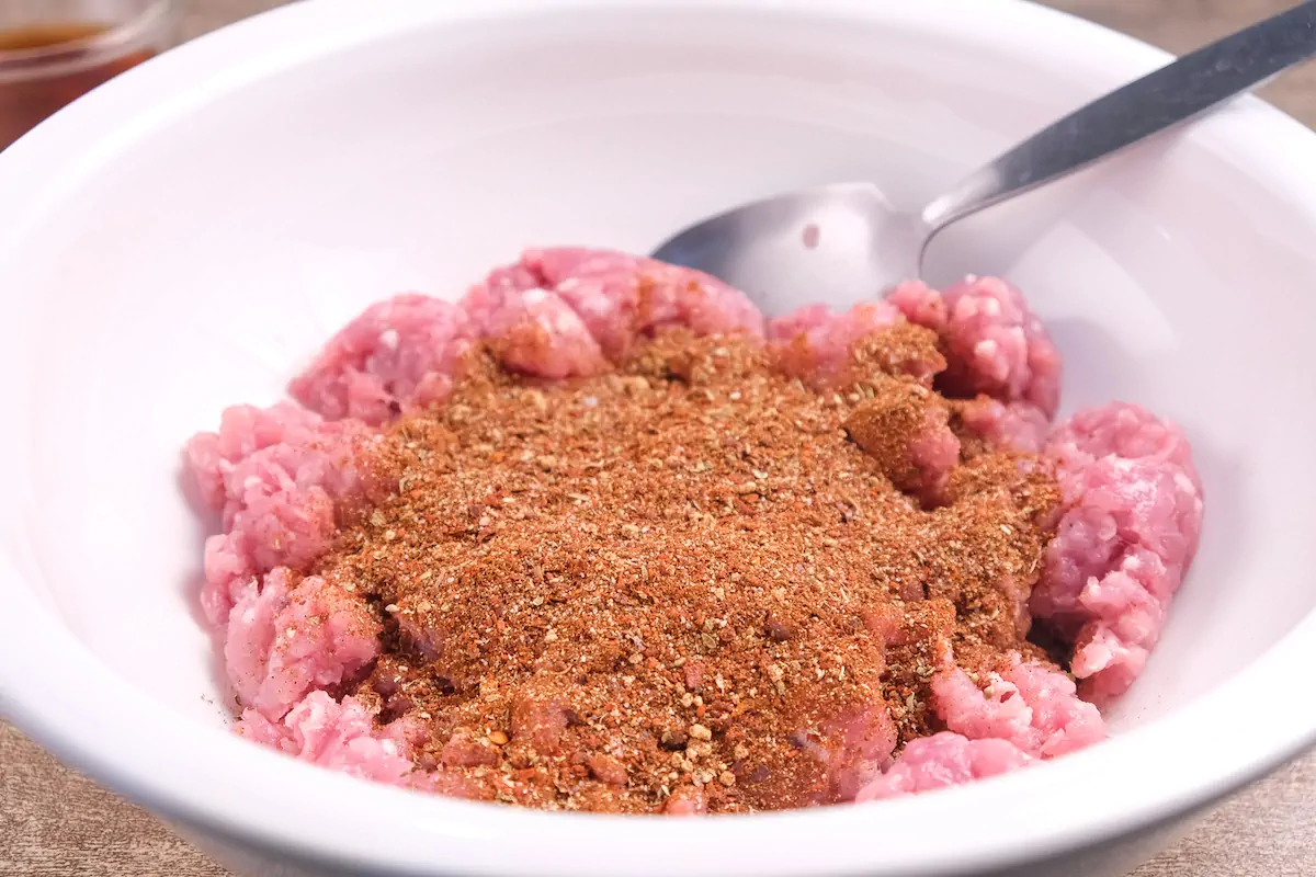 Ground pork with spice mix in a bowl.