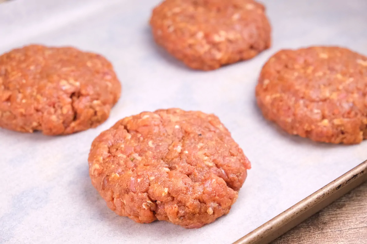 Ground pork patties in a tray lined with parchment paper ready to be cooked.