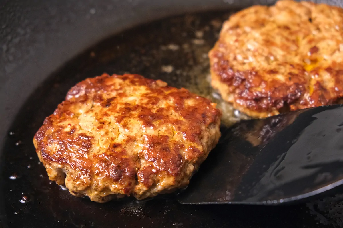 Patties getting pan fried in a cast iron skillet.