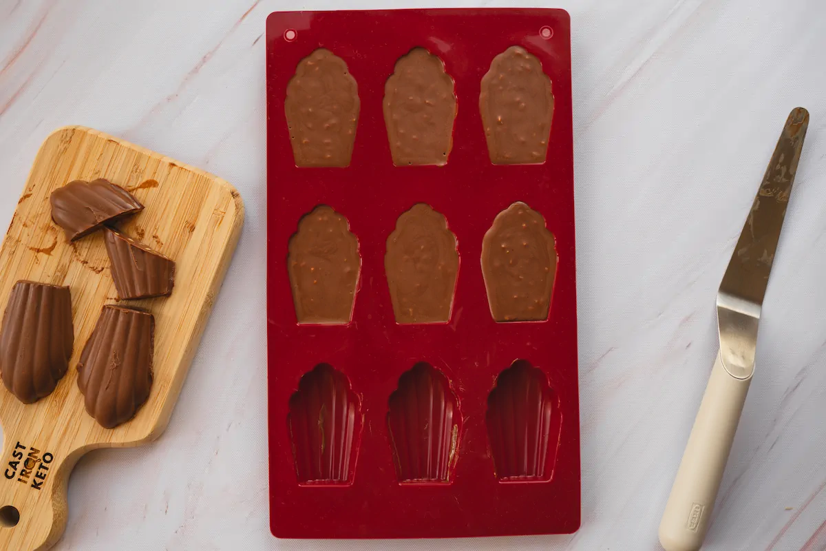 Keto chocolate fudges are displayed on a wooden board, with some removed from a silicone mold that sits partially empty.